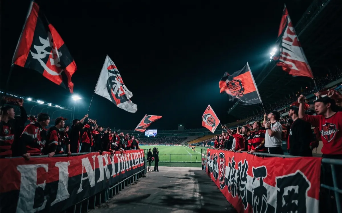 夜晚球场看台上对抗强烈的球迷分区与旗帜，强烈对比光影